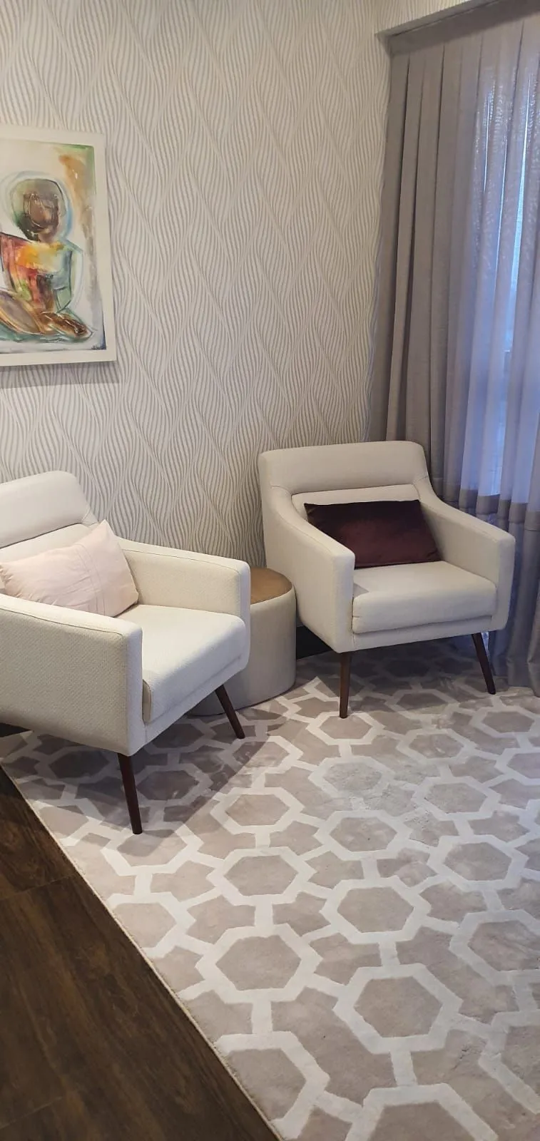 Duas poltronas claras lado a lado, com aquarela na parede, na sala de terapia de casal.