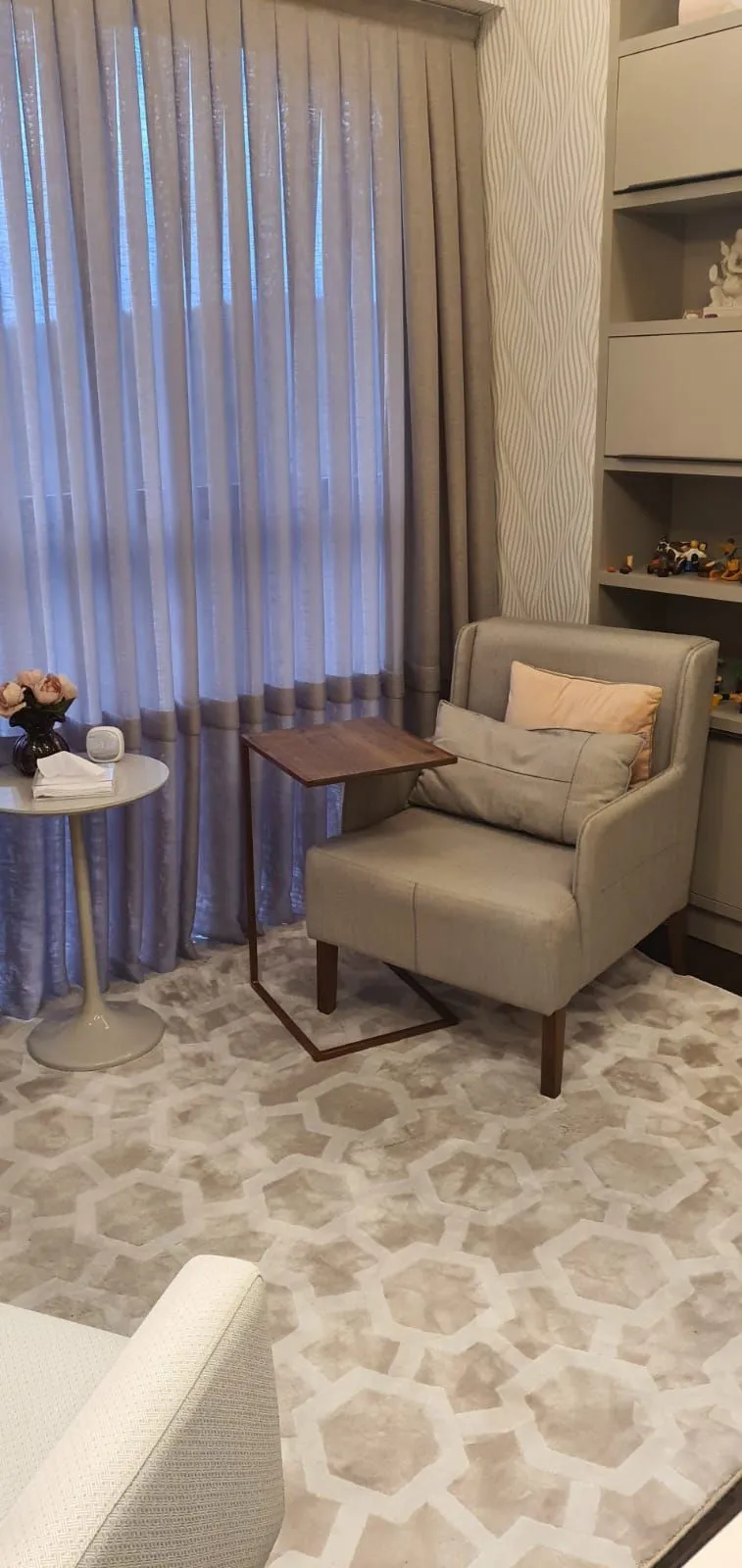Poltrona cinza com mesa de apoio de madeira e cortinas de linho, na sala de terapia sexual.